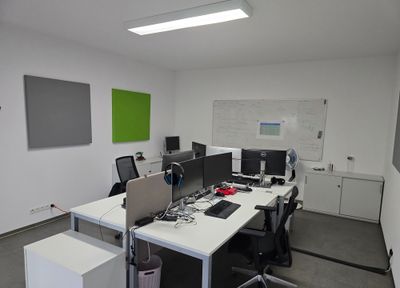 Büroraum mit Schreibtischen, mehreren Bildschirmen, Akustikpaneelen an der Wand und einem Whiteboard.