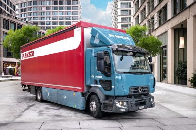 Elektro-Lastwagen von Planzer mit rotem Aufbau und petrolfarbener Fahrerkabine auf einer Strasse in Zürich.